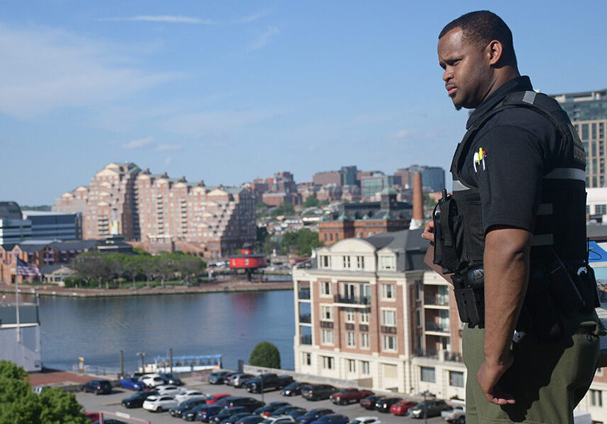 Brian Askew, in uniform, stands on the edge of Federal Hill Park, looking out over onto the Baltimore City landscape.